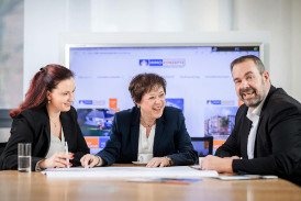 Berater und Beraterinnen der Firma ImmoKonzepte GmbH sitzen an einem Tisch im Besprechungsraum und lächeln freundlich